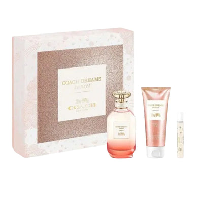A 'Coach Dreams Sunset' fragrance gift set by Coach, with a gradient pink and yellow perfume bottle, a matching body lotion, and a rollerball perfume, all elegantly presented in a glittery box with floral accents - Coach - -